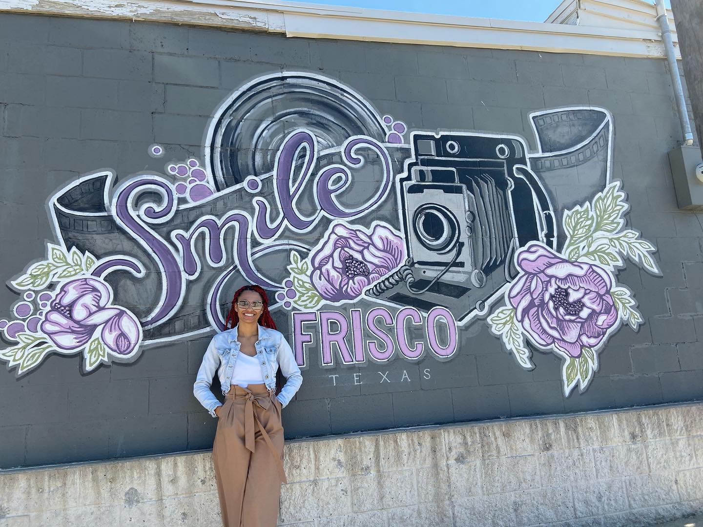 A woman standing in front of a mural of a camera that says "Smile"